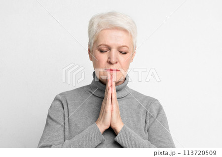 Senior closing eyes in a prayer-like gesture 113720509
