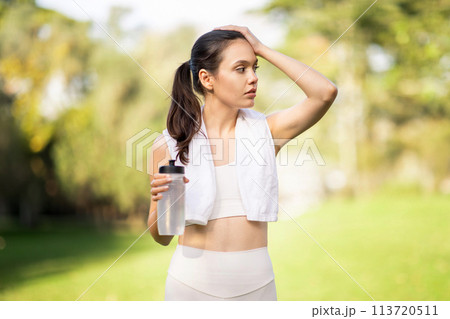An attentive young woman wipes sweat from her forehead while holding a water bottle 113720511