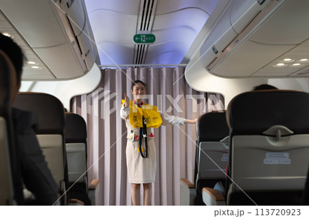 Flight attendant explaining safety regulations and showing the emergency exits to passengers on airplane cabin. Flight attendant explaining safety regulations and showing the emergency exits to passengers on airplane cabin. 113720923