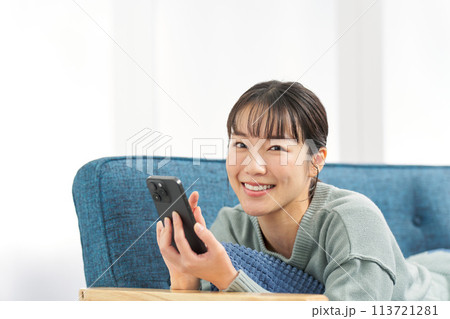 ソファで寝転んでスマートフォンを見る女性 ソファで寝転んでスマートフォンを見る女性 113721281
