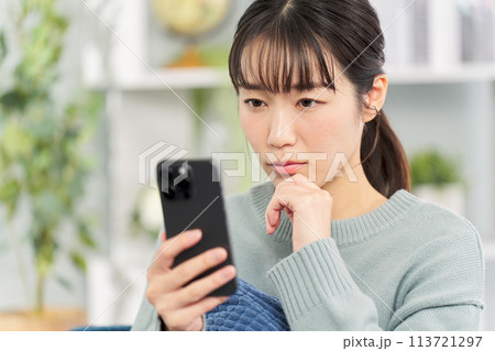 深刻な表情でスマートフォンを見る女性 深刻な表情でスマートフォンを見る女性 113721297