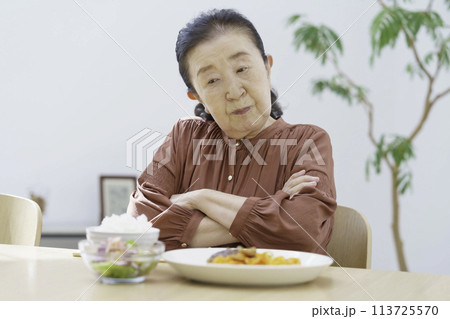 食事を前に腕組みして考えるシニア女性 113725570