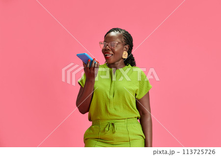 Portrait of young African-American woman talking on phone in red neon light against pastel pink studio background. Portrait of young African-American woman talking on phone in red neon light against pastel pink studio background. 113725726