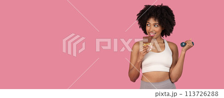 Woman eating chocolate and holding dumbbell Woman eating chocolate and holding dumbbell 113726288