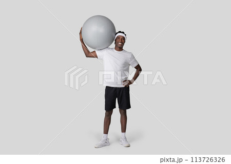 Casual man holding exercise ball at side smiling Casual man holding exercise ball at side smiling 113726326