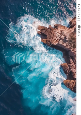 Aerial view of clean turquoise ocean waves crashing against rugged rocks Aerial view of clean turquoise ocean waves crashing against rugged rocks 113727574