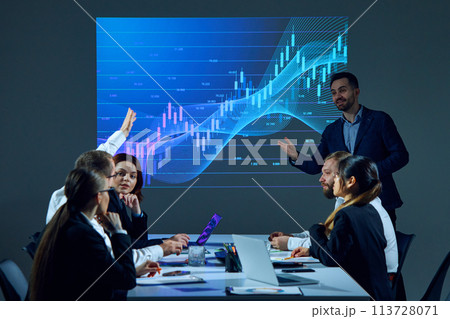 Business people gather in a conference room, discussing business strategies while examining a digital stock chart on a screen. Business people gather in a conference room, discussing business strategies while examining a digital stock chart on a screen. 113728071