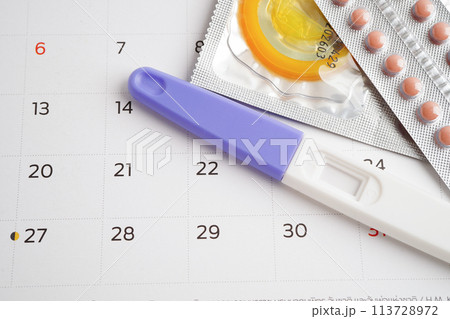 Pregnancy test with birth control pills and condom for female on calendar, ovulation day. 113728972