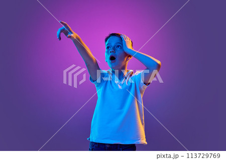 Wow. Surprised boy, in casual attire looking away and pointing to distance in neon light against purple gradient background. Wow. Surprised boy, in casual attire looking away and pointing to distance in neon light against purple gradient background. 113729769
