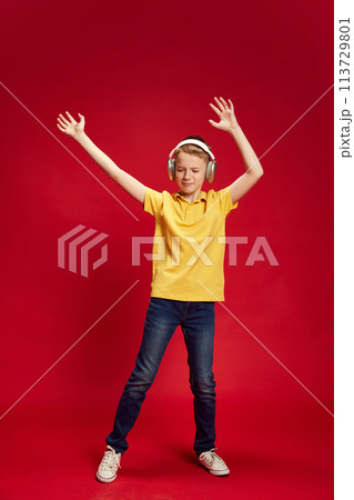Full-length portrait of teenager, dancing while listening music in headphones against red studio background. Little dancer 113729801