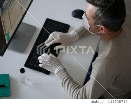 Young woman wearing protective gloves on hands and mask on face working from office or home using laptop on desk. 113730753