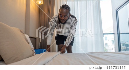Young African American man clean making bed. happy black man changing bedsheets at home standing in bedroom Young African American man clean making bed. happy black man changing bedsheets at home standing in bedroom 113731135