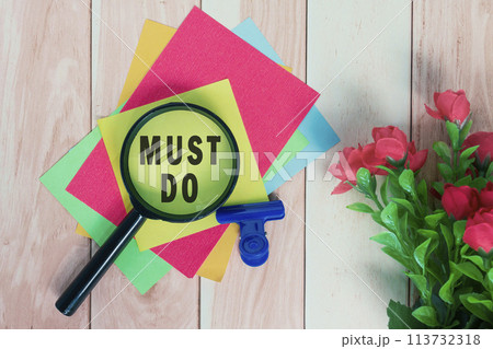 Must do word on colorful adhesive paper with magnifying glass on wooden table. Must do word on colorful adhesive paper with magnifying glass on wooden table. 113732318