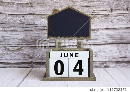 Chalkboard with June 04 date on white cube block on wooden table. 113732371
