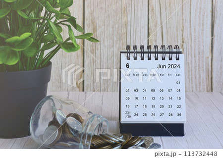 June 2024 desk calendar with stack of coins and potted plant on wooden desk. 113732448