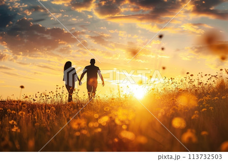 Walking loving couple in the blooming meadow. Sunset. Young couple hugging standing back outdoor. Summer field grass flowers horizon on sun background. Friendly family concept. Full length. Happy time 113732503
