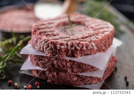 Fresh raw ground beef patties with rosemary salt and pepper made in a meat form on a cutting board 113732543