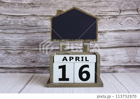 Chalkboard with April 16 date on white cube block on wooden table. 113732870