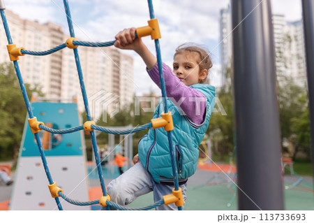 Cheerful girl 6 years old climbing the rope ladder, children's sport at playground Cheerful girl 6 years old climbing the rope ladder, children's sport at playground 113733693