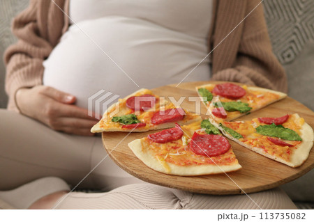 Unrecognizable pregnant woman wearing casual clothing stroking her big belly holding plate with pizza enjoying unhealthy tasty nutrition 113735082
