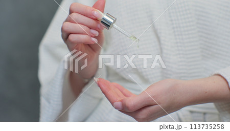 Young woman in bathrobe holding bottle, applying hyaluronic collagen vital vitamin. Applying drops of organic lotion, smooth skin. 113735258
