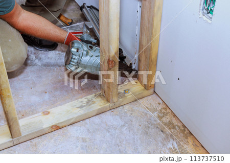 Builder is using an air hammer to nail wooden beams to a housing frame Builder is using an air hammer to nail wooden beams to a housing frame 113737510