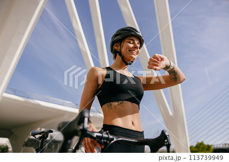 Female cyclist in helmet looking at smartwatch and counting calories burned. Healthy life concept Female cyclist in helmet looking at smartwatch and counting calories burned. Healthy life concept 113739949