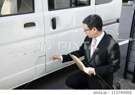 傷ついた車の修理の見積もりをする営業マン 113740808