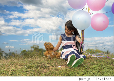 Happy Child hug teddy bear hold air balloon in green park playground. Teddy bear best friend for little kids cute girl. Autism happy playing together holding colorful helium balloons on playground Happy Child hug teddy bear hold air balloon in green park playground. Teddy bear best friend for little kids cute girl. Autism happy playing together holding colorful helium balloons on playground 113741687