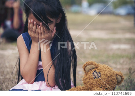 Sad girl hugging teddy bear sadness alone in green garden park. Lonely girl feeling sad unhappy sitting outdoors with best friend toy. Autism child play teddy bear best friend. Family violence concept 113741699