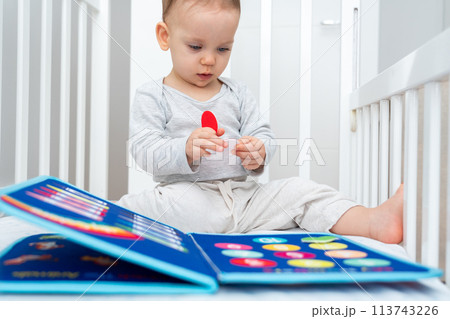 Little baby girl playing with busy book while sitting in crib. Concept of quiet books and modern educational toys 113743226