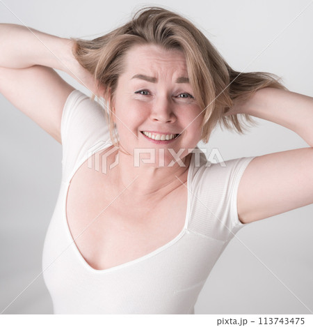 Portrait of mature adult woman with hands behind head and toothy smile. Happy woman is wearing bodysuit. High angle shot perfectly captures blonde woman's infectious energy and positive attitude 113743475