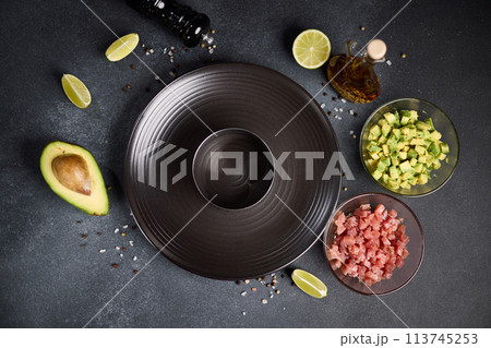 Tuna and avocado tartare recipe - sliced chopped ingredients and form on a dark table 113745253