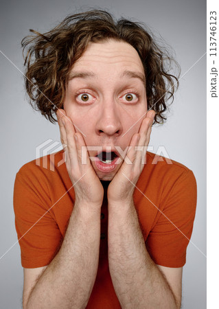 Vertical medium studio closeup of young Caucasian man with curly hair showing facial expression of astonishment 113746123