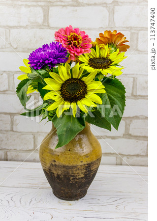 Bouquet of flowers in antique rustic clay jug against white brick wall 113747490