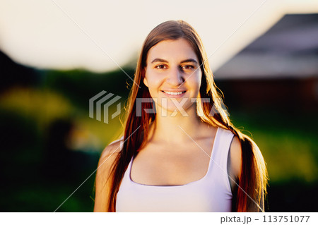 Outdoors portrait of young European woman in light of setting sun in rural area, close-up. Outdoors portrait of young European woman in light of setting sun in rural area, close-up. 113751077