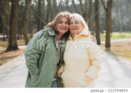 Happy loving older mature mother and daughter laughing embracing, caring young woman embracing senior middle aged mom spending time together on nature background. Woman with elderly mother in park Happy loving older mature mother and daughter laughing embracing, caring young woman embracing senior middle aged mom spending time together on nature background. Woman with elderly mother in park 113754054