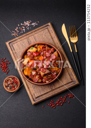 Grilled potatoes cut into slices with hunting sausages with garlic, onion 113754252