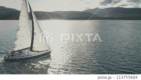 Sun over luxury yacht at ocean coast aerial. Majestic sailboat regatta race at sea bay. Sunlight flare at nobody nature serene seascape. Summer cruise at Brodick harbor, Arran island, Scotland, Europe 113755684