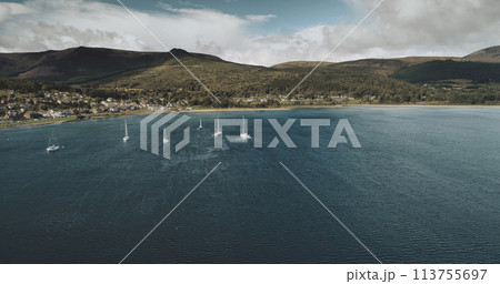 Scotland's sailboats ocean seascape aerial view in coastal water of Brodick Bay. Ships and boats near shore with homes, cottages, roads at greenery valleys. Scottish cityscape scenery shot 113755697