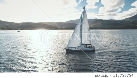 Brodick Harbour, Arran Island, Scotland. Slow motion sun reflection at sails of yacht aerial. Nobody nature landscapeSunny seascape with white sailboat at ocean bay. Mountain sea coast Brodick Harbour, Arran Island, Scotland. Slow motion sun reflection at sails of yacht aerial. Nobody nature landscapeSunny seascape with white sailboat at ocean bay. Mountain sea coast 113755754