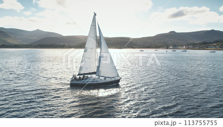 Brodick Harbour, Arran Island, Scotland. Slow motion sun reflection at sails of yacht aerial. Nobody nature landscapeSunny seascape with white sailboat at ocean bay. Mountain sea coast 113755755