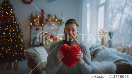 Person holding a red heart in a cozy room, decorated for Valentine's Day with a tree and lights. Person holding a red heart in a cozy room, decorated for Valentine's Day with a tree and lights. 113756098