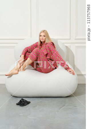 Barefoot woman in pink pyjama sitting on couch Barefoot woman in pink pyjama sitting on couch 113757968
