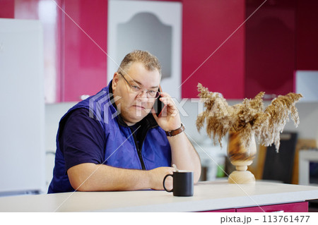 Large white man in his 40s using smartphone to communicate while sitting in front of kitchen island. Large white man in his 40s using smartphone to communicate while sitting in front of kitchen island. 113761477
