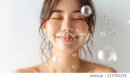 A woman displays a radiant smile with soap covering her face, embodying a moment of blissful relaxation and care for her skin. 113762245