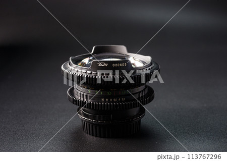 Stacked vintage camera lenses with a focus on the serial number, reflective glass surface, photography tools against a dark gradient background. 113767296
