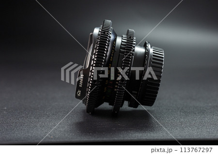 Side view of antique camera lens with distinct engravings and focus dials, part of a photography collection, against a moody dark background 113767297