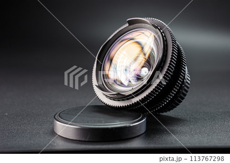 Tilted vintage camera lens on display, colorful light reflection on glass, detailed focus mechanism, photography gear against a dark background 113767298