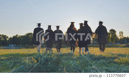 College graduates walk at sunset holding hands. 113770607